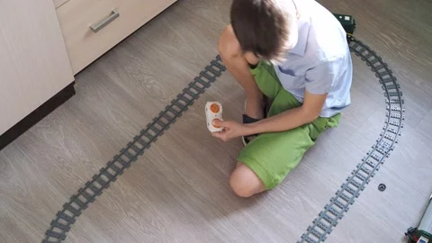 A boy in a shirt is playing with a train on the controls on the floor in the Stock Footage 170566180
