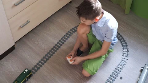 A boy in a shirt is playing with a train on the controls on the floor in the Stock Footage 171289029