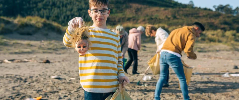 Boy showing doll head while cleaning the beach Stock Photos