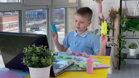 Boy shows paper Easter colorful diy bunnies while chatting online on a laptop. Stock Footage 171974523