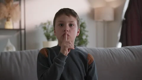 Boy Shushing Gesture on Couch. Innocent child quiet gesture relaxed home scene Stock Footage 335483257
