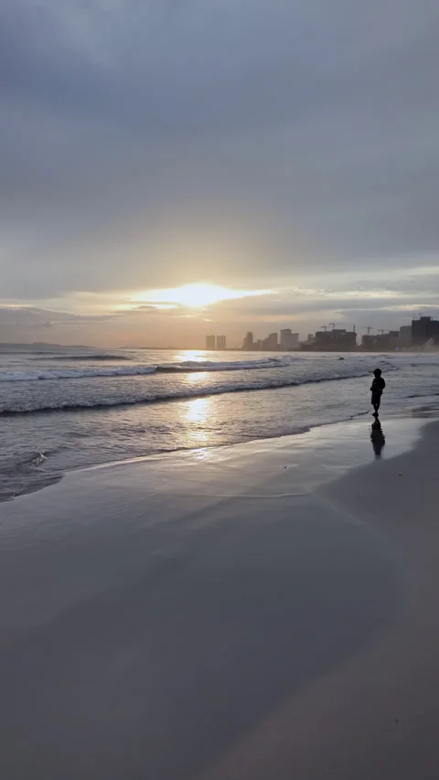 A boy, silhouetted by a shimmering sunset path to a distant city. Stock Footage 313316557
