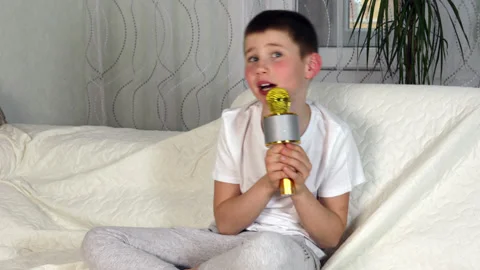 Boy singing with microphone, dancing with hands sitting on sofa Stock Footage 154312422
