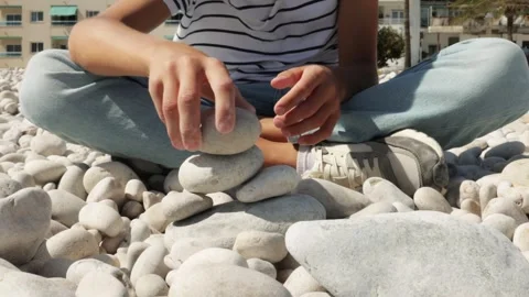 Boy Sit Cross Legged, Stacking Smooth Stones on Pebble Beach, Enjoy Peacefu.. Stock Footage 286977170