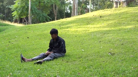 A boy sits alone on the green grass next to the remains of burnt garbage Video stock 338166648