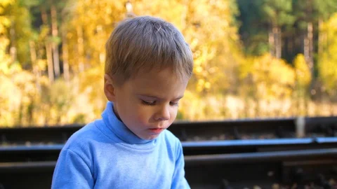 The boy sits and eats a bun on the railway tracks. Autumn warm day. Vidéo 96810225
