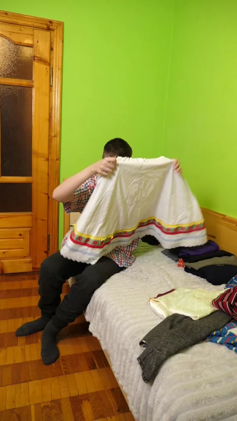 A boy sits on the bed folding clothes, organizing his room and neatly arrangi Stock Footage 323367506