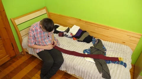 A boy sits on the bed folding clothes, organizing his room and neatly arrangi 動画素材 323367590