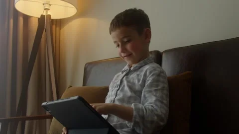 The boy sits on the bed, playing or watching a movie over the Internet using a Stock Footage 308001316