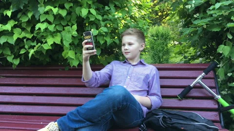 A boy sits on the bench and makes selfie Stock Footage 64027952
