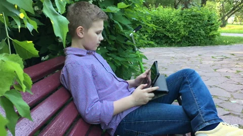 Boy sits on a bench and playing on the tablet Stock Footage 64026870