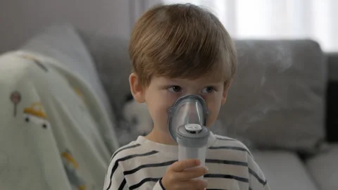 Boy sits calmly on a couch, holding a nebulizer mask for therapy Stock Footage 293588885