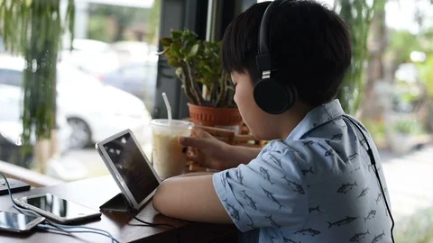 Boy Sits on chair Using Tablet wearing headphones. Vidéo 87674551