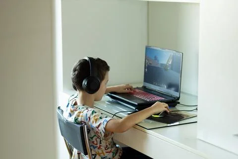 The boy sits at the computer and plays from the game, The child's free time. Stock Photos