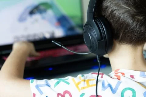 The boy sits at the computer and plays from the game, The child's free time. Stock Photos