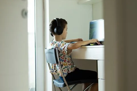 The boy sits at the computer and plays from the game, The child's free time. Stock Photos