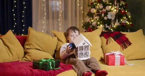 Boy sits on couch and opens door of toy Christmas house Stock Footage 316749109