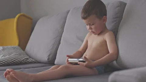 Boy sits on couch playing handheld console joy of carefree childhood and Video stock 280032685
