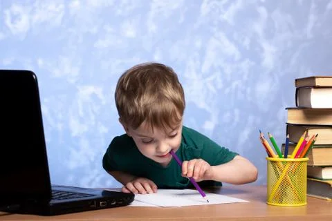 Boy sits at a desk with books and a laptop, draws with his left hand a pencil Stock Photos