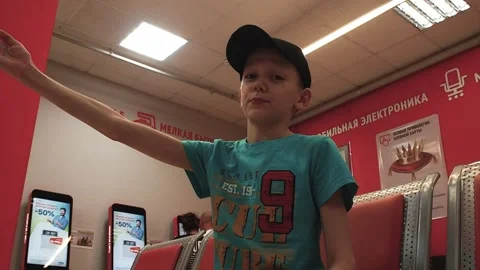 A boy sits in an electronics store and shows with his hand Stock Footage 201837398