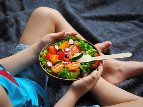 A boy sits on the floor and eats a delicious green salad 스톡 사진