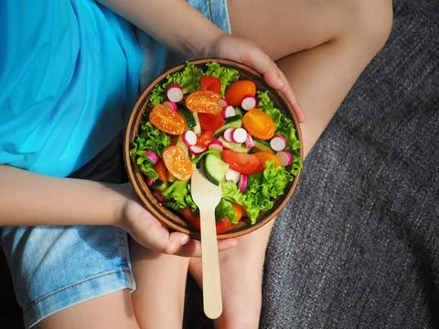 A boy sits on the floor and eats a delicious green salad 스톡 사진