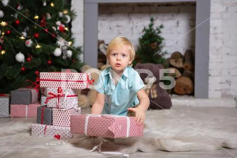 Boy sits on the floor by the Christmas tree. stacks boxes by the fireplace. Stock Photos