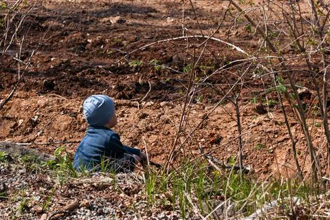 A boy sits on the ground in a park Stock Photos