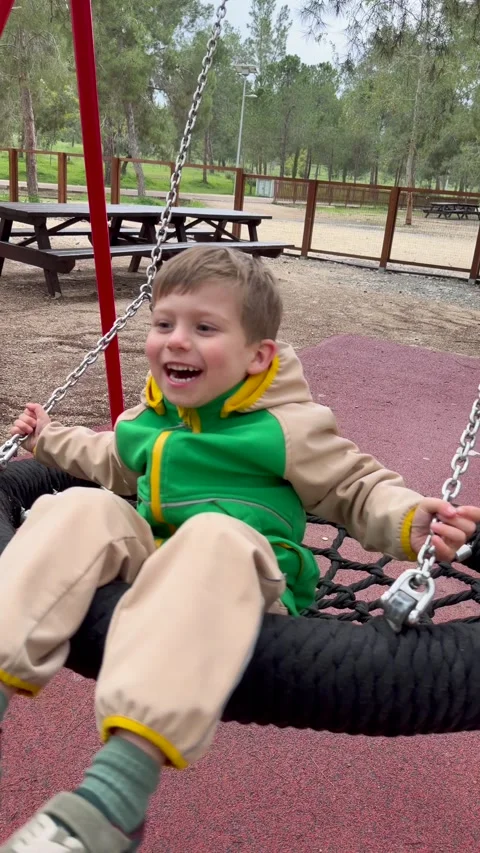 Boy sits inside round nest swing on modern playground with red rubber surface Stock-Footage 334704304