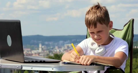 The boy sits at a laptop, writes data in a notebook and looks into a monocula Stock Footage 136541271