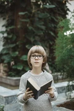 A boy sits in a library and reads a book against the background of living plants Stock Photos