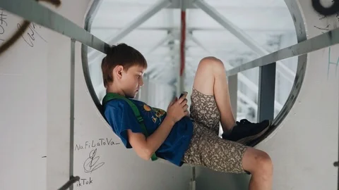 The boy sits on metal structures under the bridge. Walk around town Stock Footage 113071940