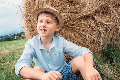 Boy sits near big haystack on the field Stock Photos