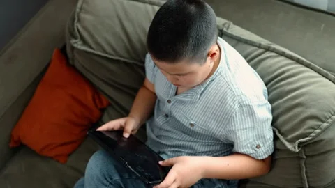 Boy sits on olive couch with digital tablet in blue striped shirt, indoor Video stock 312661782