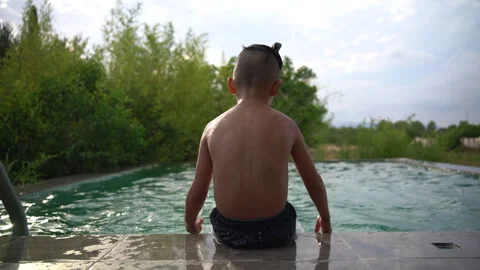 Boy Sits at Pool Edge Splashing Water at Sunset Stock Footage 343358489