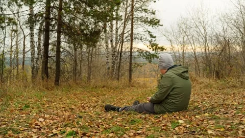 A boy sits resting on the top of a mountain strewn with autumn yellow leaves. Stock Footage 319062414