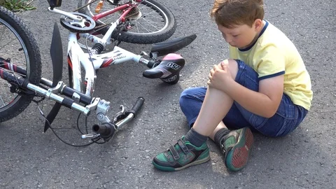 Boy sits in a road after falling from a bike, calms the pain in her knee Video stock 94556886