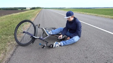 Boy sits in a road after falling from a bike, calms the pain in her knee Video stock 111523599
