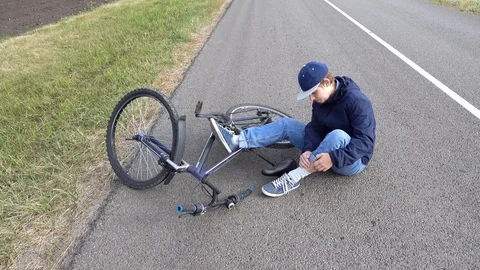 Boy sits in a road after falling from a bike, calms the pain in her knee Video stock 111523631