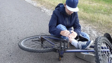 Boy sits in a road after falling from a bike, calms the pain in her knee Stock Footage 111523669