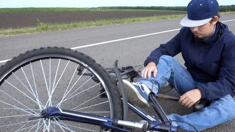 Boy sits in a road after falling from a bike, calms the pain in her knee Video stock 111523758