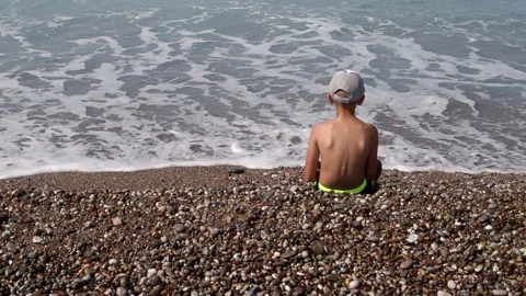A boy sits by the sea and throws stones. FullHD footage Stock Footage 162401928