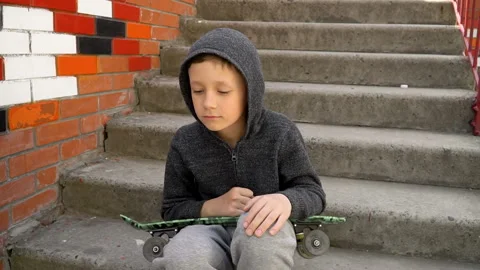 The boy sits on the steps and holds a skateboard in his hands Stock Footage 107068108