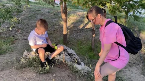 Boy sits on a stone and shows his mother a leaf he found while they take a break Stock Footage 317081659