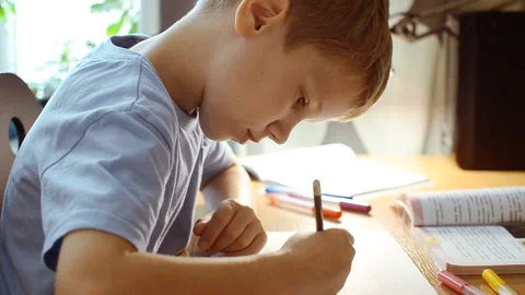 The boy sits at the table and draws a pencil on a piece of paper. Video stock 95654765