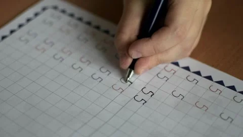 A boy sits at a table and writes numbers in a notebook with his left hand Stock Footage 291861173