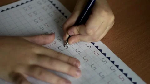 A boy sits at a table and writes numbers in a notebook with his left hand Stock Footage 291861191