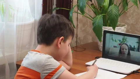 A  boy sits at the table writing homework notebook computer to study School Stock Footage 158457274