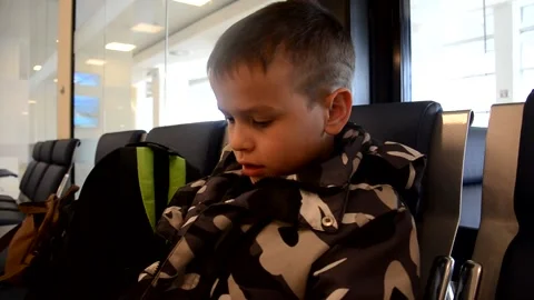 A boy sits at a train station or aroport while waiting for a train or plane Stock Footage 143611478