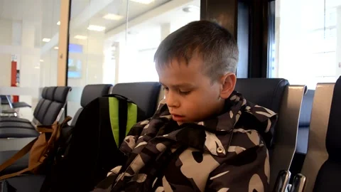 A boy sits at a train station or aroport while waiting for a train or plane 库存影片 143611483